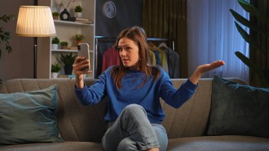 Mavi kazaklı mutlu bir kadın telefonuyla konuşurken gülümsüyor, koltukta rahatça oturuyor..