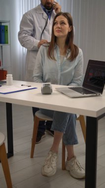 Bir tıp uzmanı bir hastayı muayene etmek için steteskop kullanır, sağlık hizmetleri uygulamalarını vurgular.