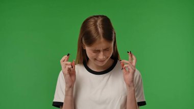 Gençlik duyguları konsepti. Genç kız kameraya poz veriyor, parmaklarını çapraz yapıyor ve beklenen yüz ifadesi, bekleyen yüz ifadesi, krom anahtar yeşil ekran arka plan modelinde izole edilmiş..