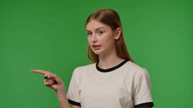 Gençlik duyguları konsepti. Genç kız kameraya poz veriyor gülümsüyor ve parmağıyla işaret ediyor, pozitif ifade, krom anahtar yeşil ekran arka plan modelinde izole edilmiş..