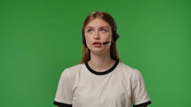 Kulaklıklı genç bir kız canlı yeşil bir arka planda dikkatle dinliyor gibi görünüyor..