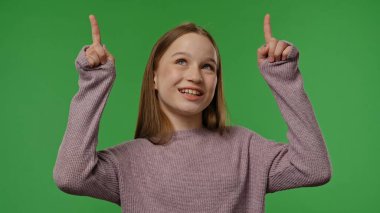 Gençlik duyguları konsepti. Genç kız kameraya poz veriyor, parmaklarını havaya kaldırıyor, pozitif ifade, krom anahtar yeşil ekranda izole edilmiş, arka plan modeli..
