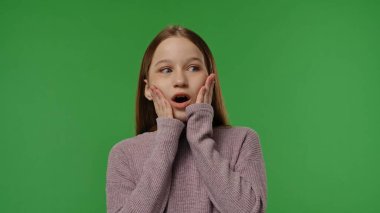 Gençlik duyguları konsepti. Genç kız kameraya el ele poz veriyor. Şaşırtıcı bir şekilde gülümsüyor, olumlu bir ifade veriyor. Krom anahtar yeşil ekran arka plan modelinde izole edilmiş..