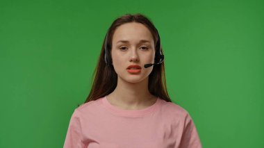 Kulaklıklı genç bir kız canlı yeşil bir arka planda dikkatle dinliyor gibi görünüyor..