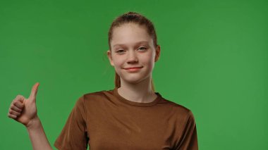 Gençlik duyguları konsepti. Kameraya gülümseyen ve başparmağını jest gibi gösteren genç bir kız, pozitif ifade, krom anahtar yeşil ekran stüdyo arka planında izole edilmiş.