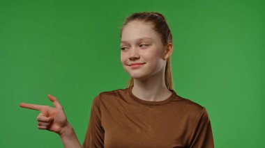 Gençlik duyguları konsepti. Genç kız kameraya poz veriyor gülümsüyor ve parmağıyla işaret ediyor, pozitif ifade, krom anahtar yeşil ekran arka plan modelinde izole edilmiş..