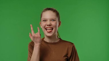 Gençlik duyguları konsepti. Kameraya gülümseyen ve rock hareketi gösteren genç kız, pozitif ifade, krom anahtar yeşil ekran arka plan modelinde izole edilmiş..