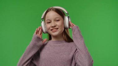 Gençlik duyguları konsepti. Kameraya poz veren genç bir kız kulaklıkla müzik dinliyor, dans ediyor, pozitif ifade ediyor, krom anahtar yeşil ekran arka plan modelinde izole edilmiş. Yavaş çekim