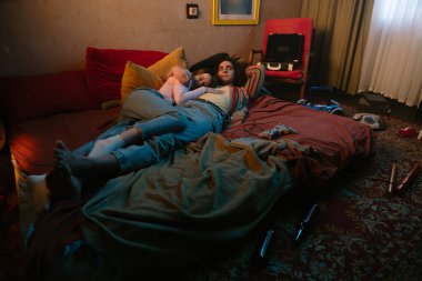 İki insan rahat bir yatakta rahatlar. Etrafları minderlerle çevrili ve sıcak, davetkar bir atmosfer yaratıyorlar..