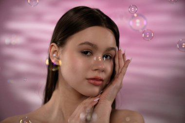 Yüzen kabarcıklar arasında, yumuşak pembe bir arka plana karşı yumuşak, sükunet ve zarafeti vurgulayan genç bir kadını yakalayan güzel bir portre..