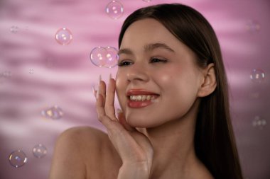 Genç bir kadın, etrafında kabarcıklar uçuşurken neşeyi ifade eder. Yumuşak pembe bir arkaplan üzerine kurulur. Huzurlu bir anın altını çizer..