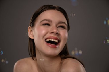 Stüdyo ortamındaki genç bir kadın, etrafında küçük sabun köpükleri dolaşırken neşeyle gülüyor..