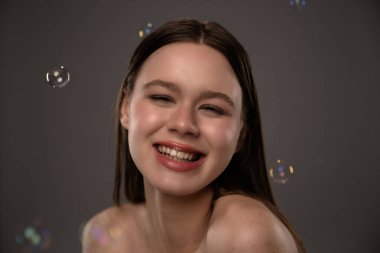 Etrafında kabarcıklarla neşeyle gülümseyen genç bir kadın neşeli ve neşeli bir atmosfer yaratıyor..