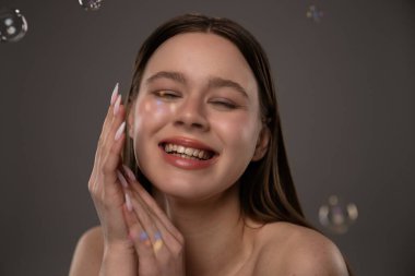 Gözleri kapalı neşeli bir kadın, doğal güzellik ve mutluluk sergiliyor. Hassas sabun köpükleri neşeli bir dokunuş ekler.