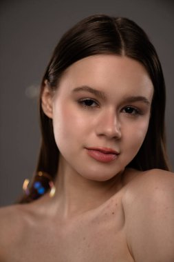 Bir görüntüde, doğal güzelliğini vurgulayan pürüzsüz, makyajlı genç bir kadın görülüyor..