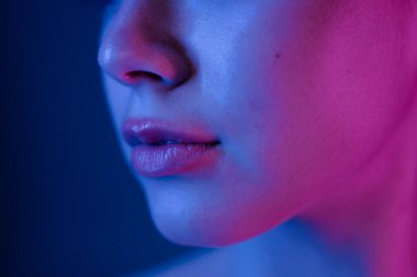 Bir kadının yüzünün canlı pembe ve mavi ışıkla aydınlatıldığı, yüz hatlarının ve deri dokusunun aydınlatıldığı yakın plan bir portre görüntüsü..