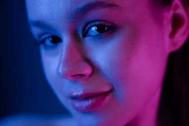 Canlı mavi ve mor neon ışıklarıyla yıkanmış bir kadının yakın plan portresi onun özelliklerini ön plana çıkarıyor..