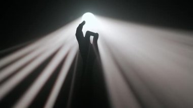 Sisli karanlık stüdyoda sahne ışıklarının içindeki kişi. Parlak sıcak spot ışıkları, karanlıkta dönen profesyonel ışıklandırma ekipmanları, el silueti ışık ışınlarına parmaklarıyla dokunuyor..