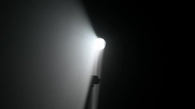 Sisli karanlık stüdyoda sahne ışıklarının içindeki kişi. Parlak beyaz spot ışıkları, karanlıkta parlayan profesyonel ışıklandırma ekipmanları, el silueti dumanla ve ışıkla dokunup oynuyor..