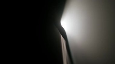 Sisli karanlık stüdyoda sahne ışıklarının içindeki kişi. Parlak beyaz spot ışığı, profesyonel ışıklandırma ekipmanları sağ tarafta karanlıkta parlıyor, el silueti dumanla ve ışıkla dokunuyor ve oynuyor..