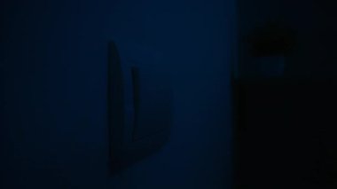 Bir kişi ışıkları açmak için duvardaki ışık düğmesine basıyor ve enerji tasarrufu eylemlerini gösteriyor. Yaklaşın, ağır çekim.