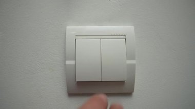 Bir kişi ışıkları söndürmek için duvardaki bir ışık düğmesine basıyor ve enerji tasarrufu eylemlerini gösteriyor. Yaklaşın, ağır çekim.