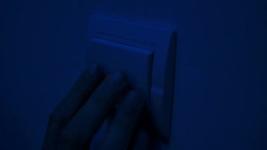 Bir el loş ışıklı bir odada, sakinleştirici mavi bir renkle yıkanmış bir ışık düğmesini açmak için uzanır. Yaklaşın, ağır çekim.