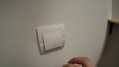 Bir kişi ışıkları söndürmek için duvardaki bir ışık düğmesine basıyor ve enerji tasarrufu eylemlerini gösteriyor. Yaklaşın, ağır çekim.