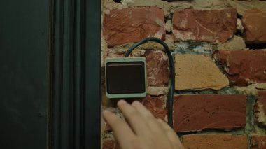 Bir el tuğla bir duvara monte edilmiş bir düğmeye basıyor, düşük ışık ortamında aydınlatılıyor, gizemli bir atmosfer yaratıyor. Yaklaşın, ağır çekim.