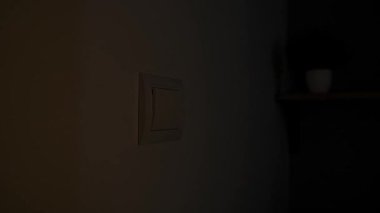 Elektrik kesintisi sırasında yakınlarda bir mum yanıp sönerken bir kişi düşük ışıkta ışık düğmesine uzanır. Kapat.