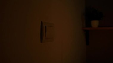 Elektrik kesintisi sırasında yakınlarda bir mum yanıp sönerken bir kişi düşük ışıkta ışık düğmesine uzanır. Kapat.