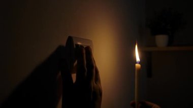 Elektrik kesintisi sırasında yakınlarda bir mum yanıp sönerken bir kişi düşük ışıkta ışık düğmesine uzanır. Kapat.