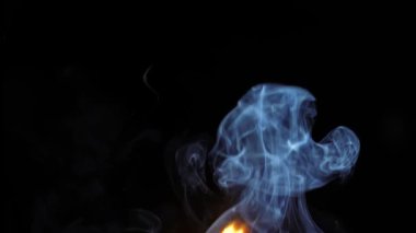 Derin siyah bir zıtlık ve hareket gösteren, kıvrımlı mavi duman ve sıcak alevin büyüleyici bir görüntüsü..