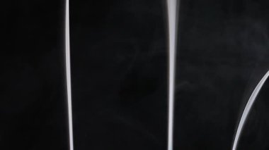 Karanlık bir arka plan karşısında dumanı andıran zarif dikey çizgilere sahip soyut bir görüntü, bir gizem hissi uyandırıyor. Yavaş çekim