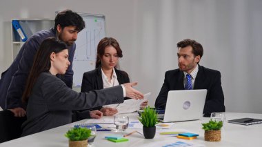 Ofiste bir iş toplantısına katılan dört profesyonel, çizelgelerle stratejiyi tartışıyor..