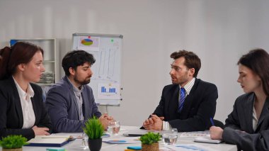 Ofiste bir iş toplantısına katılan dört profesyonel, çizelgelerle stratejiyi tartışıyor..
