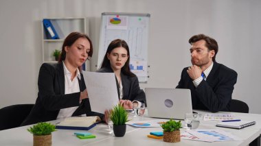 Ofiste bir iş toplantısına katılan üç profesyonel, çizelgelerle stratejiyi tartışıyor..