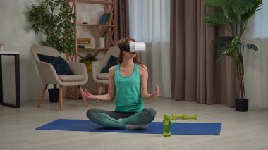 Bir kadın VR kulaklığı kullanarak yoga yapıyor, farkındalık ve teknolojiyi birleştirerek sağlıklı yaşam deneyimi sağlıyor..