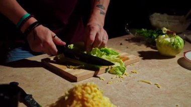 Bir şef, ahşap kesim tahtasının üzerinde taze yeşil marul dilimler, yiyecek hazırlama becerileri sergiler..