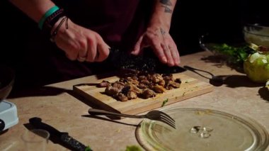 Bir insan ahşap kesme tahtasındaki malzemeleri ustalıkla doğrayarak taze ürünlerle lezzetli bir yemek hazırlar..