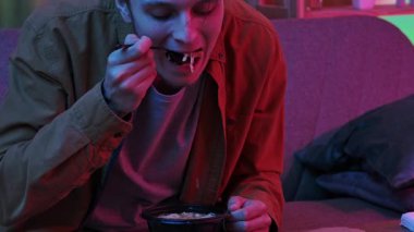 Evde Asya fast food 'unun tadını çıkarıyorum. Akşamları evde, kanepede oturan, Asya yemeği siparişi veren, elinde kaşık tutan ve miso çorbası içen genç bir adam, zevkten dört köşe. Yavaş çekim.