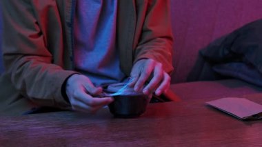 Evde Asya fast food 'unun tadını çıkarıyorum. Genç adam akşamları kanepede oturuyor, lezzetli Asya yemeği siparişi veriyor, kaseden plastik ambalajı çorba ile çıkarıyor, kaseyi açıyor ve aroma kokuyor..