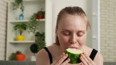 Sağlıklı gıda reklamı konsepti. Evdeki kanepede oturan ve taze vitamin meyvesi yiyen olgun karpuz dilimlerini yiyen, çiğneyen ve gülümseyen, atıştırmanın tadını çıkaran genç bir kadın. Yavaş çekim.