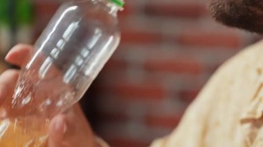 Abur cubur reklamı konsepti. Yetişkin stili sakallı bir adam masada oturmuş elinde bir şişe limonata, şişeyi sallıyor ve bir yudum alıyor, lezzetli fast food tatlı içkisinin tadını çıkarıyor. Yavaş çekim.