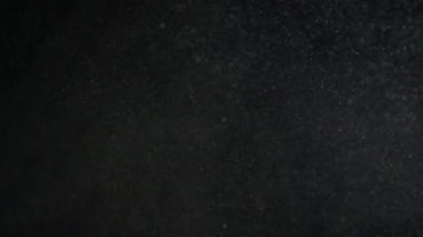 Dumanlı havada rastgele uçan küçük toz bulutu, nesneler için boş uzay şablonu. Beyaz toz bulutundaki pek çok toz parçacığı boş siyah zıtlık arka planında yüzüyor. Yavaş çekim.