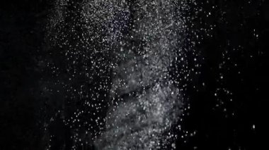 Dumanlı havada rastgele uçan küçük toz bulutu, nesneler için boş uzay şablonu. Birçok toz parçacığı beyaz toz yukarıdan düşüyor, boş siyah zıtlık arka planında yüzüyor. Yavaş çekim.