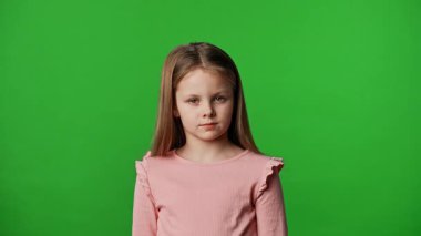 Çocuk duyguları reklam konsepti. Tişörtlü küçük kız kameraya bakıyor ve göz kırpıyor, nötr bir ifade, krom anahtar yeşil ekranda izole edilmiş arka plan modeli..