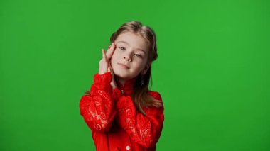 Çocuk duyguları reklam konsepti. Gülümseyen kız çocuğu kameraya poz veriyor, yüzlerine dokunuyor ve sevimli jestler yapıyor, olumlu ifade veriyor, krom anahtar yeşil ekran arka plan modelinde izole edilmiş..