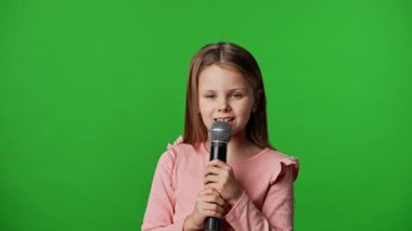 Çocuk duyguları reklam konsepti. Gülümseyen kız çocuğu karaoke mikrofonunda şarkı söylüyor, pozitif ifade, krom anahtar yeşil ekranda izole edilmiş arka plan modeli..