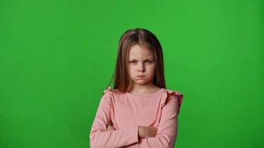 Çocuk duyguları reklam konsepti. Suratı asık ve kollarını kavuşturmuş küçük kız kameraya bakıyor, krom anahtar yeşil ekran stüdyo arka planında izole edilmiş..